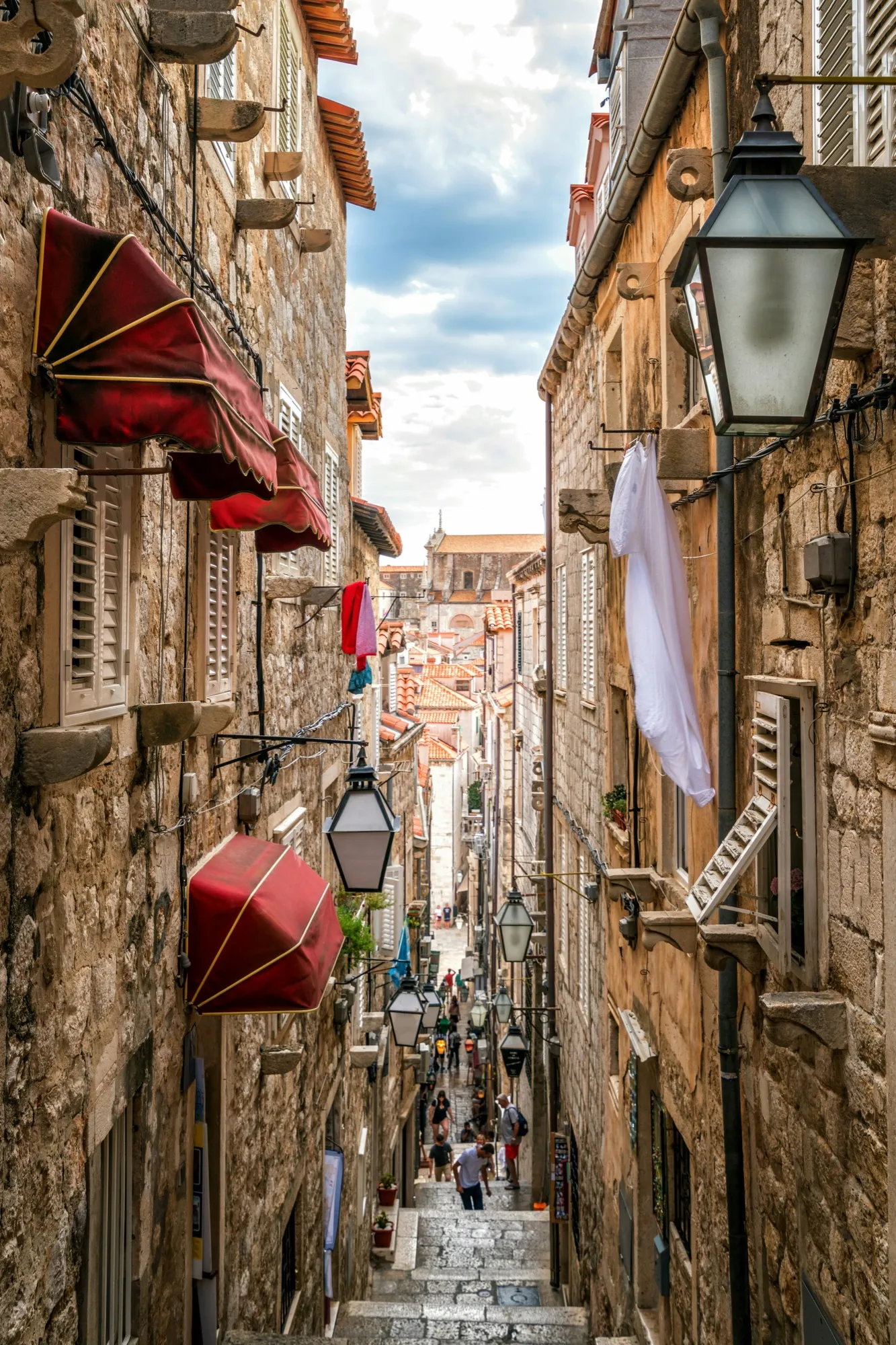 A narrow stepped street in Dubrovnik's old town, lanterns and flags overhead
