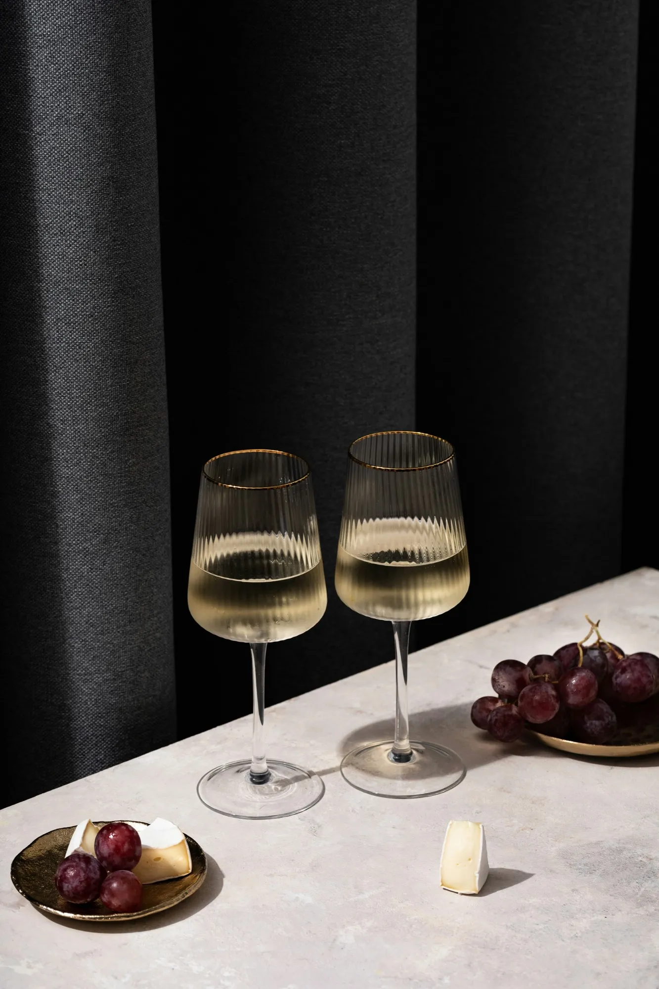 Two glasses of white wine with grapes and cheese at a tasting table